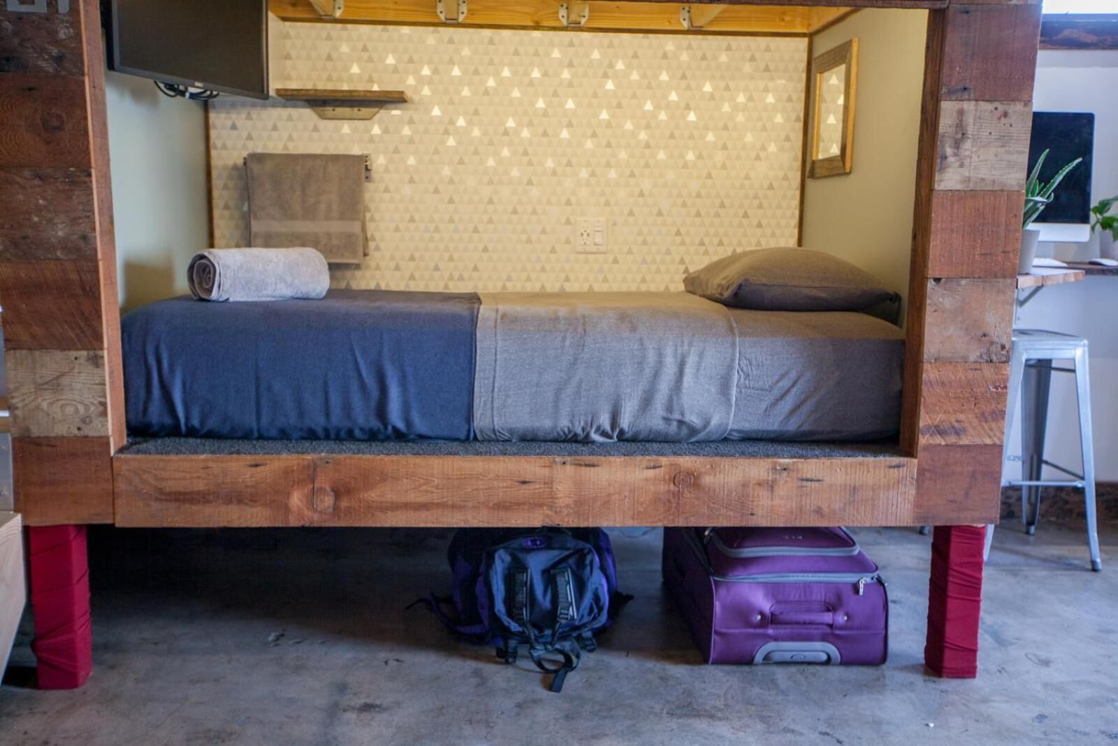 A small, rustic-style room with a wooden bed frame, a desk, and a chair.