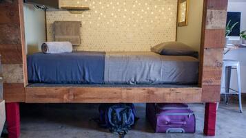 A small, rustic-style room with a wooden bed frame, a desk, and a chair.