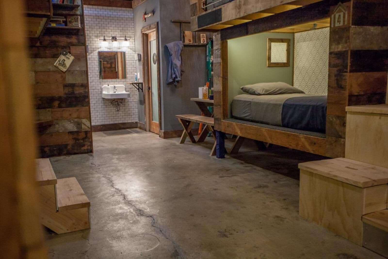 A rustic room with a bunk bed, a small table, a sink, and a staircase.