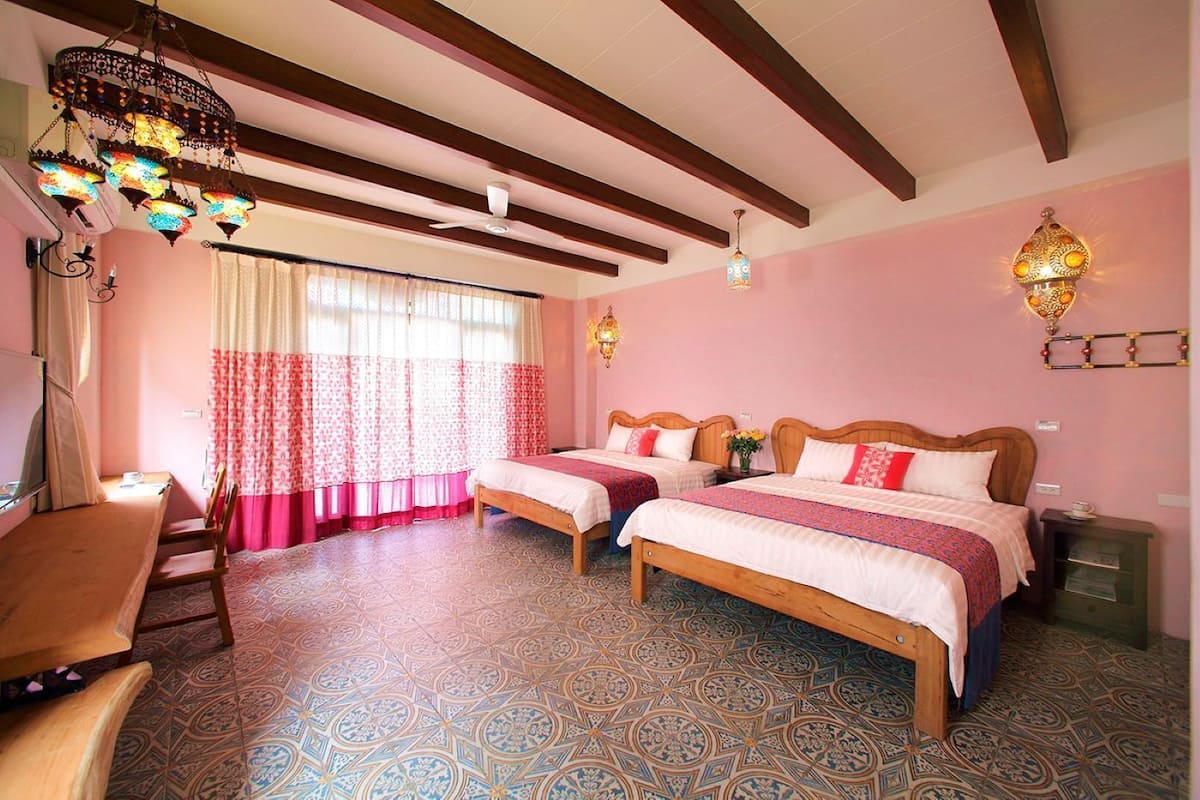 A room with two wooden beds, a desk, a chair, patterned floor tiles, and a ceiling fan.