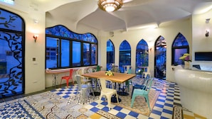 A dining area with a checkered floor, a wooden table, and chairs. There are windows with decorative glass and a chandelier.