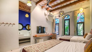 A bedroom with two beds, a desk, a television, and a bathroom with a mirror and sink.
