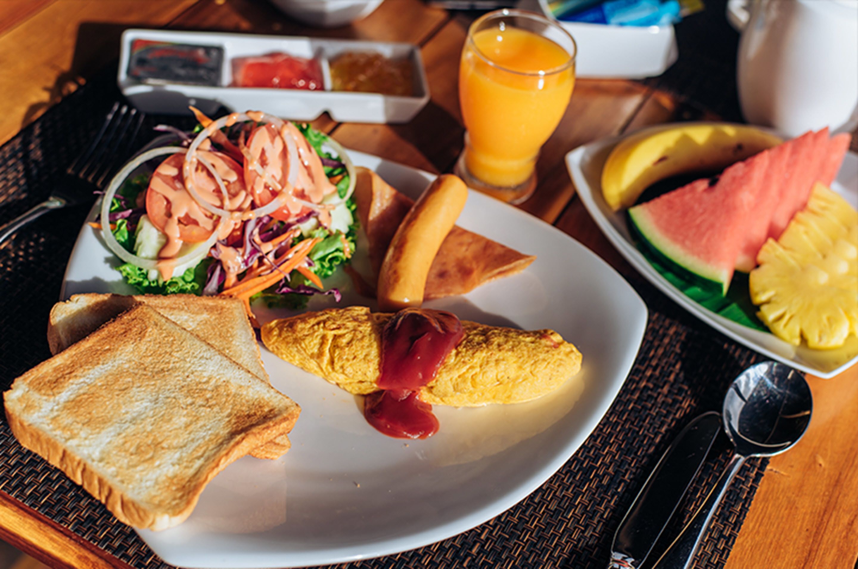 A breakfast plate with toast, an omelet, a salad, and fruit.