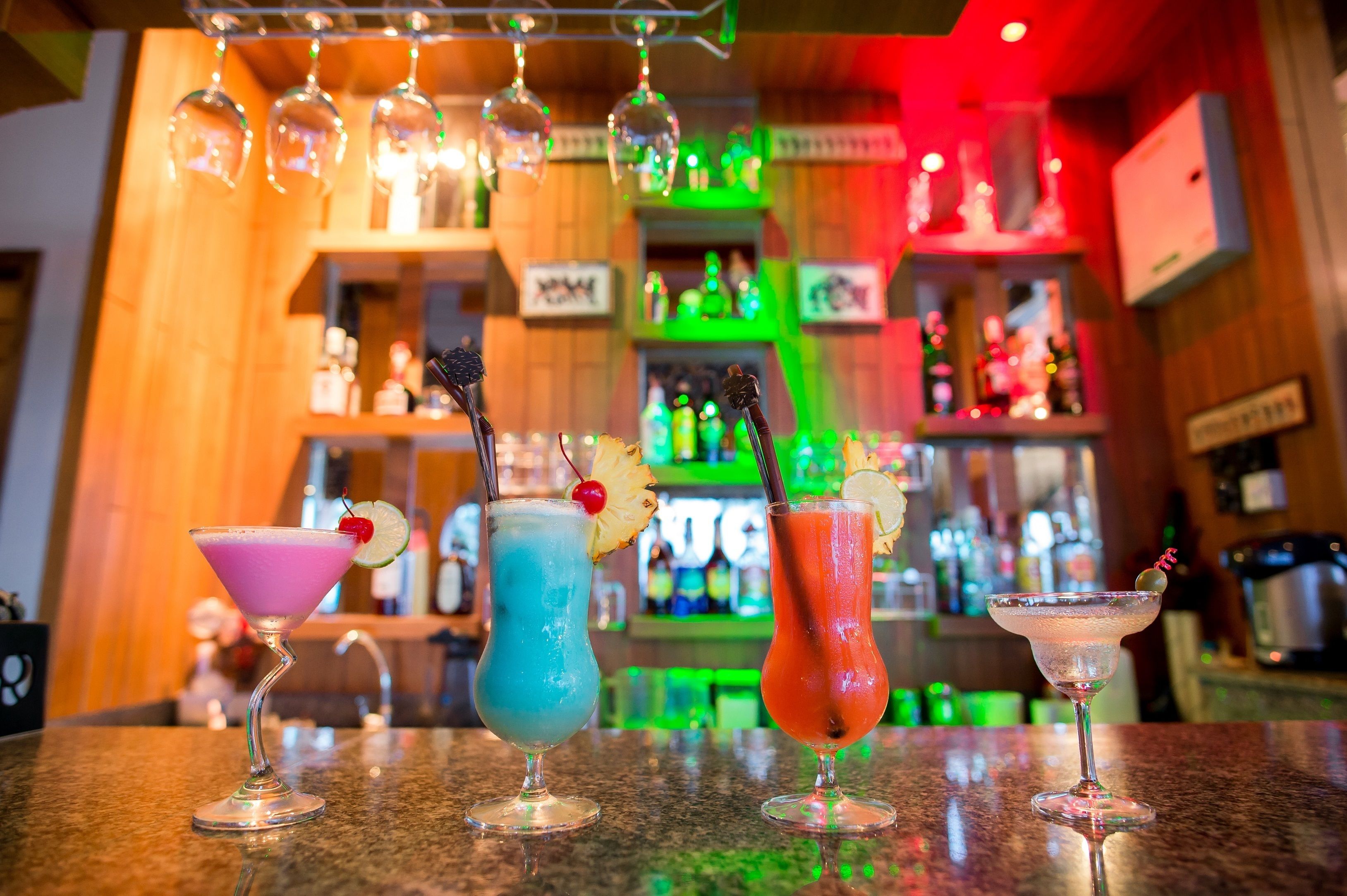 Three cocktails on a bar counter with a wooden interior and shelves of bottles in the background.