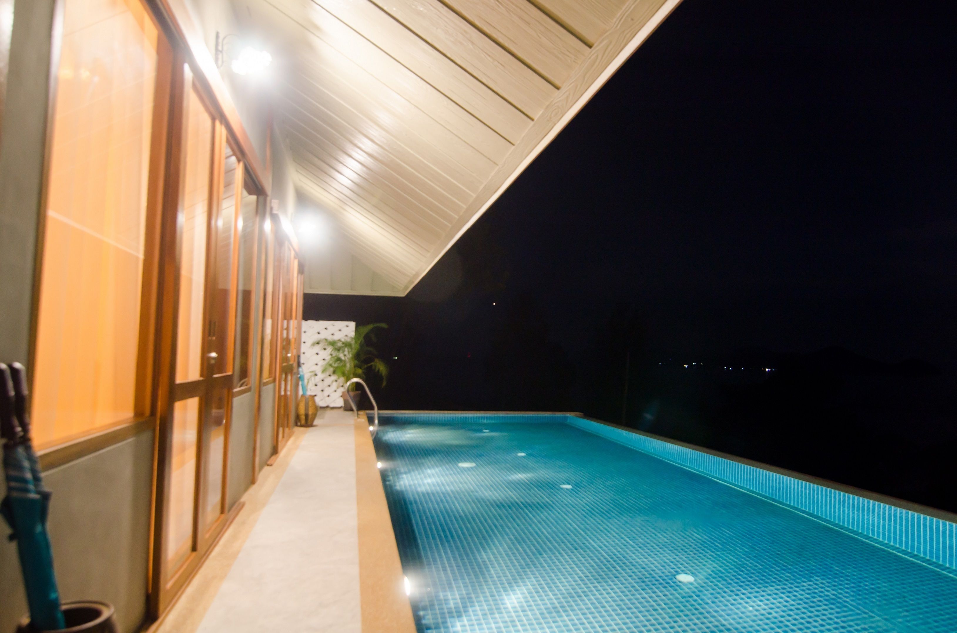 Vista nocturna de una piscina con piso de azulejos y techo de madera.