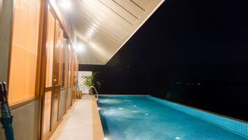 Vista nocturna de una piscina con piso de azulejos y techo de madera.