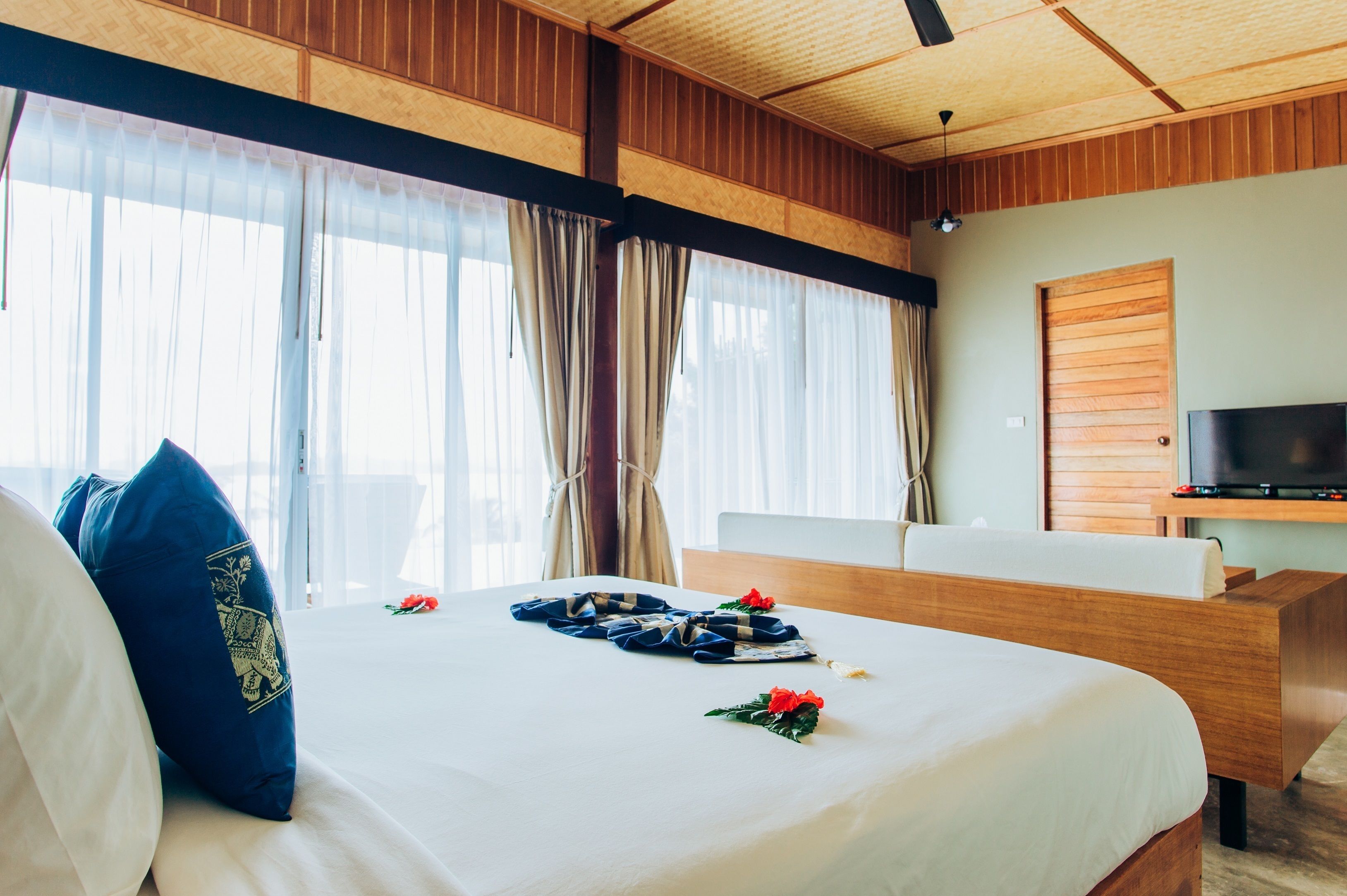 Une chambre d’hôtel avec un grand lit, une tête de lit en bois, un téléviseur posé sur un meuble en bois et une fenêtre avec des rideaux.