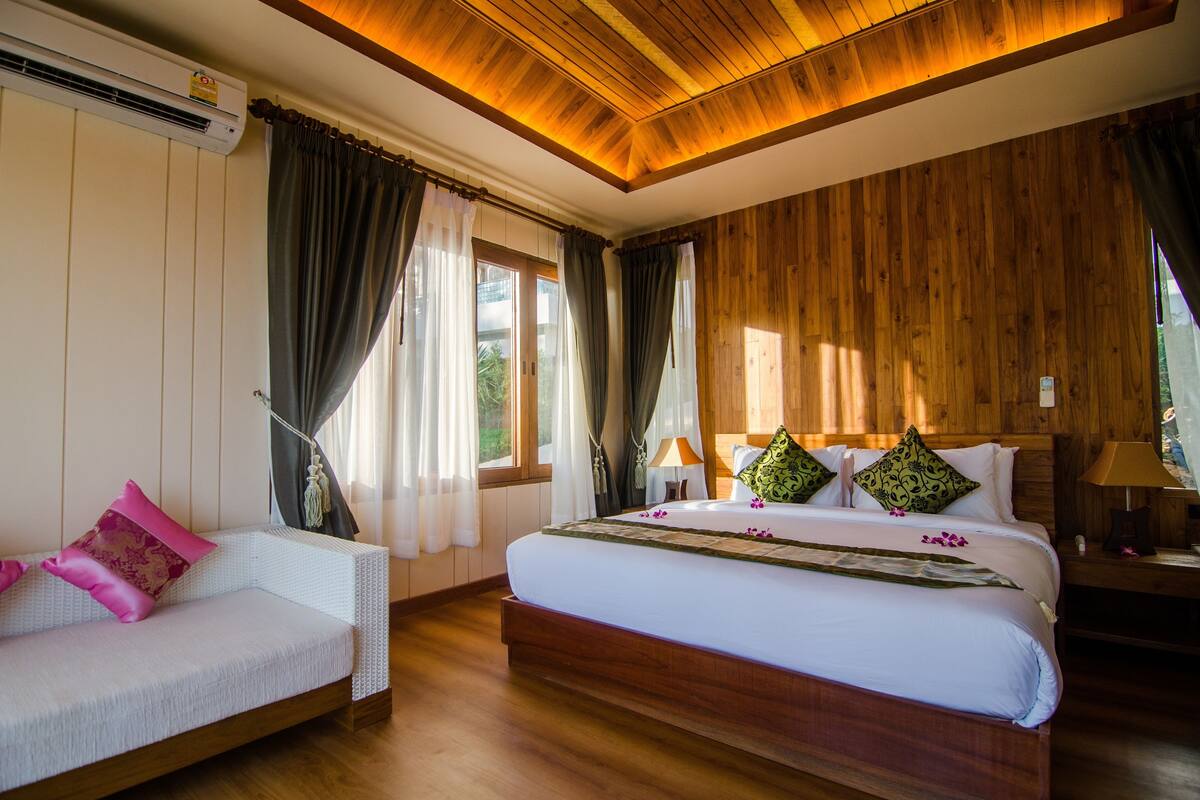 Une chambre à coucher avec un lit, un canapé, un lambris en bois, un ventilateur de plafond et une fenêtre avec des rideaux.