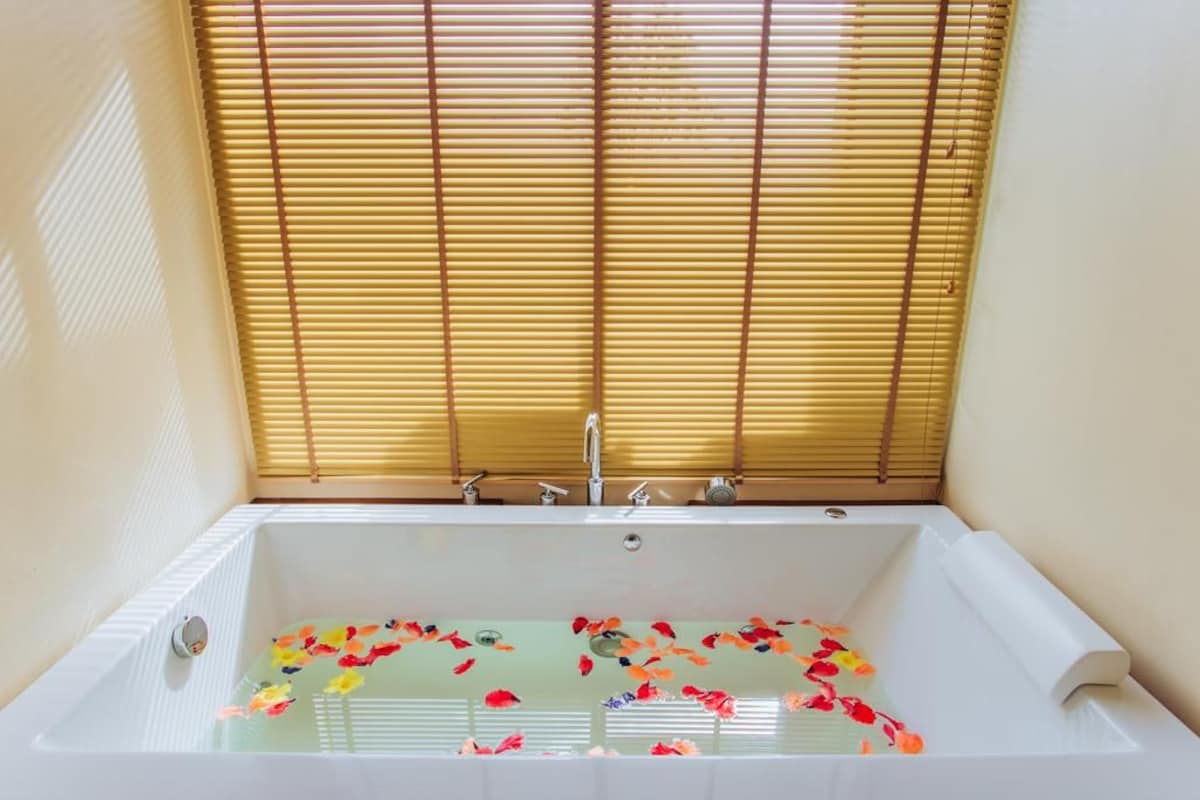 A bathtub with a window above it, a towel, and flower petals in the water.