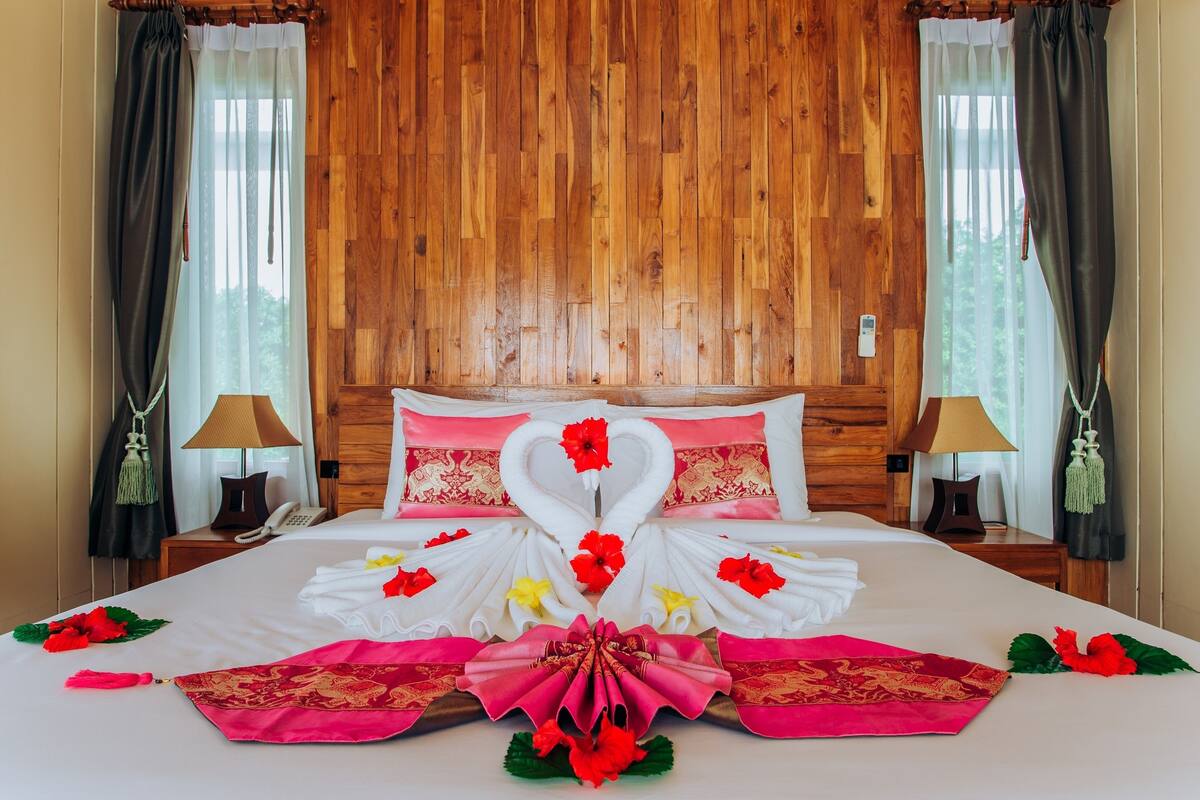 Une chambre d’hôtel avec une tête de lit en bois, un lit soigneusement fait et agrémenté de compositions florales, ainsi que deux tables de chevet avec des lampes.
