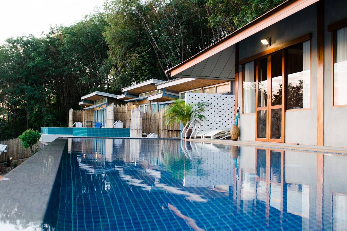 Une piscine dotée d’une terrasse en bois et de chaises longues, entourée d’une clôture en bois et d’arbres.