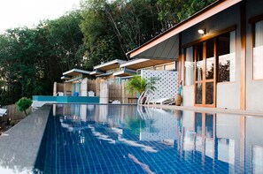 Ein Pool mit Holzboden und Liegestühlen, umgeben von einem Holzzaun und Bäumen.