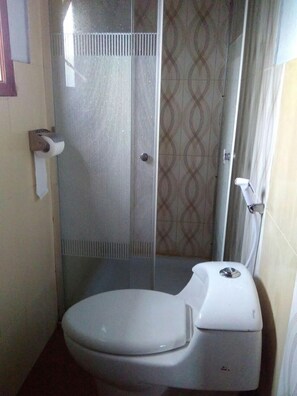 A small, enclosed bathroom with a toilet, a shower stall, and a toilet paper holder. - Jazzi Homestay (Wonokitri)