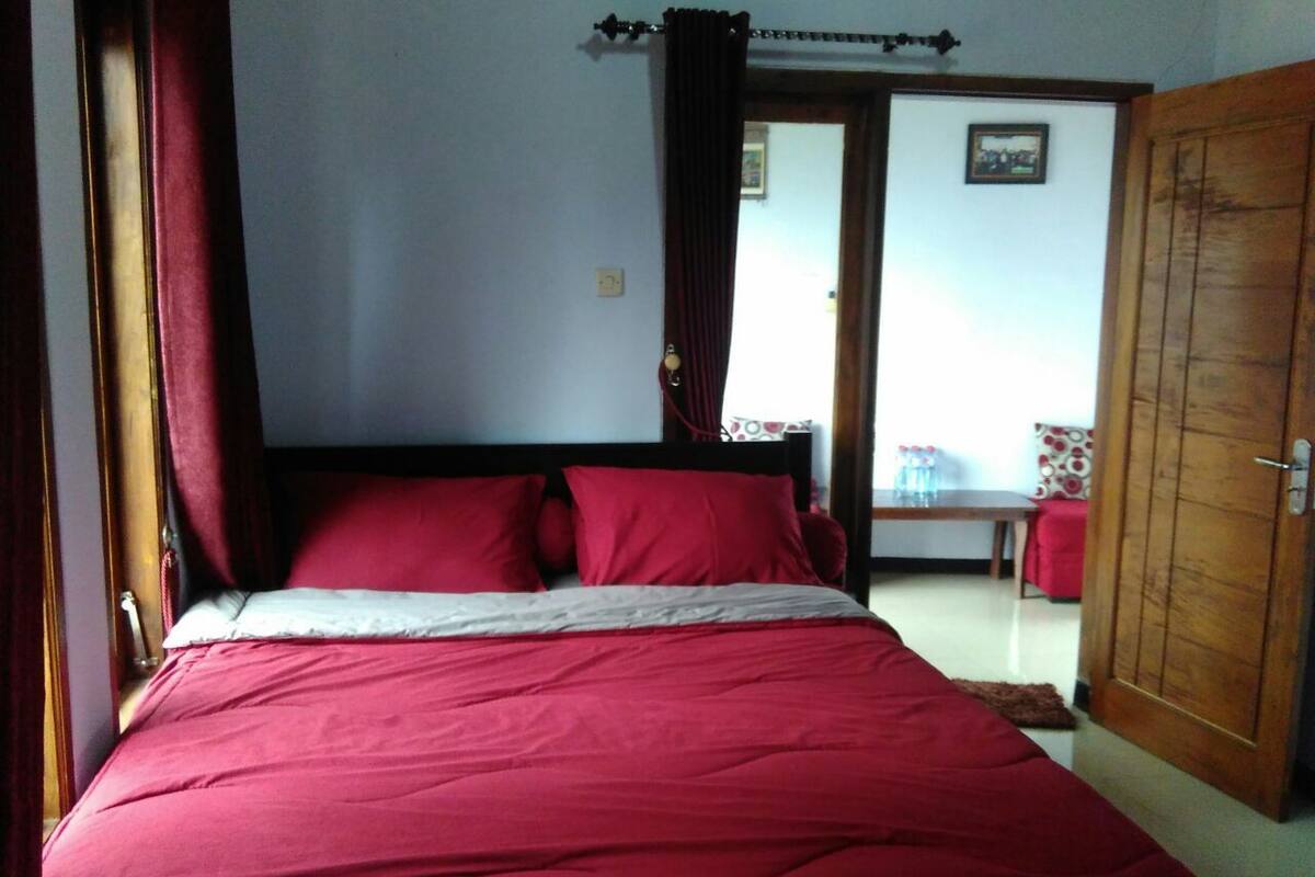 A bedroom with a large bed, a wooden wardrobe, and a door leading to another room.