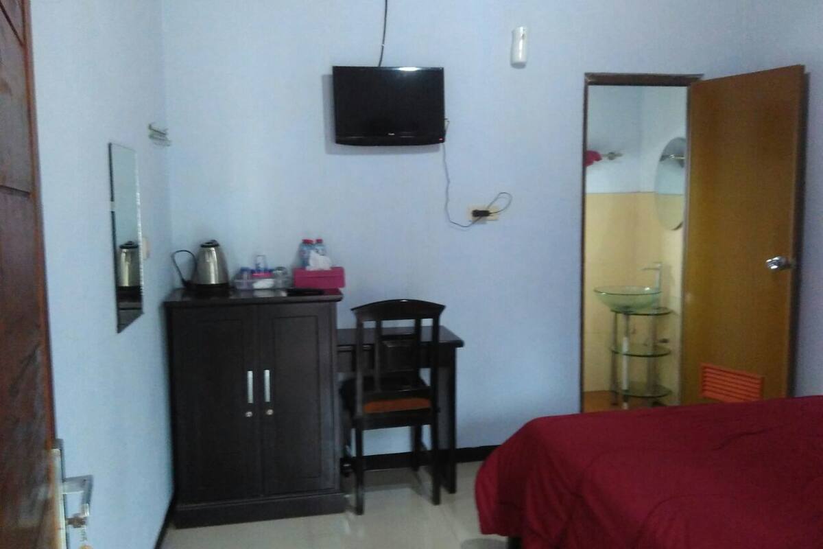 A small room with a bed, a desk with a chair, a television mounted on the wall, and a wardrobe.