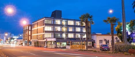 A multi-story hotel with a modern design, featuring a ground-level restaurant and a parking area.