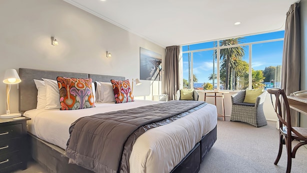 A modern hotel room with a large bed, a desk, and a view of palm trees.