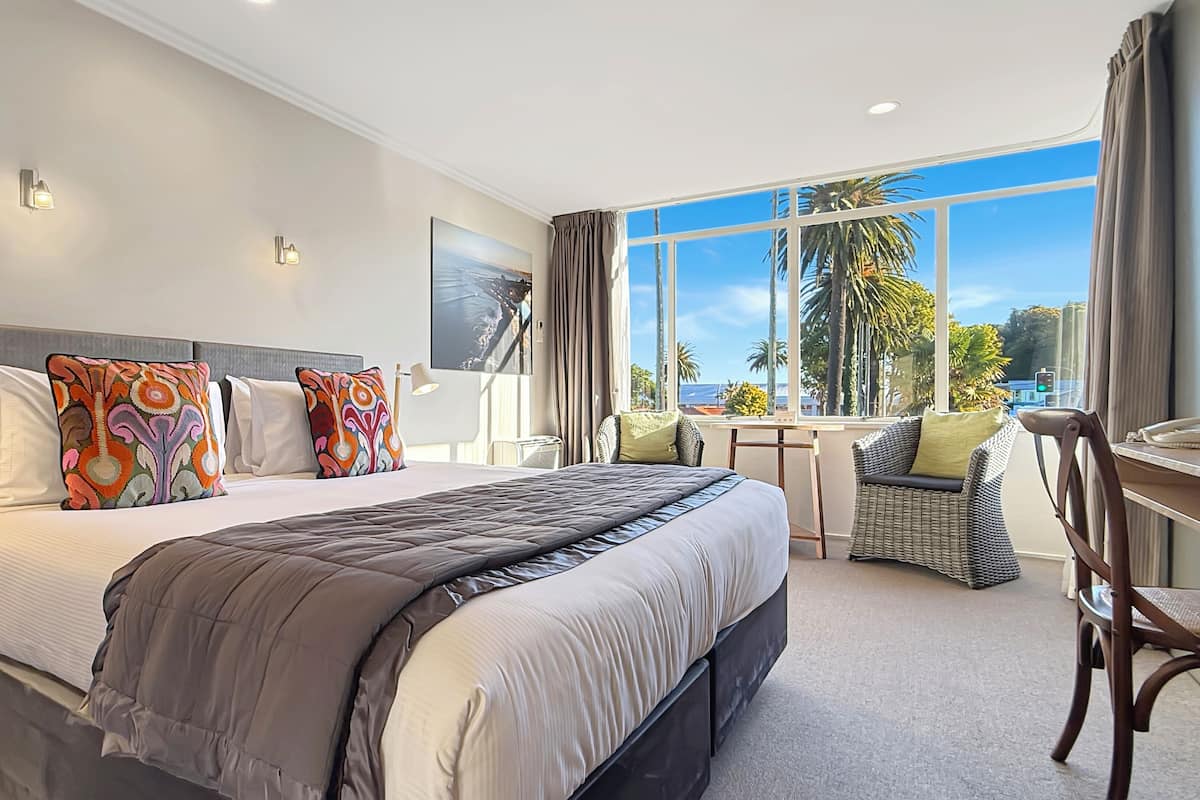 A modern hotel room with a large bed, a desk, and a view of palm trees.