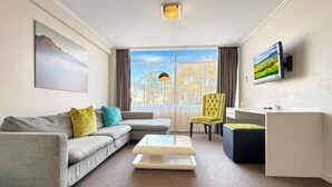 A modern living room with a grey sofa, a coffee table, a yellow armchair, and a TV mounted on the wall.