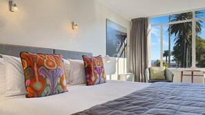 A hotel room with a large bed, two colorful pillows, a view of palm trees, and a painting on the wall.