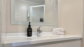 A bathroom with a white sink, a mirror, a bottle of hand soap, and a stack of towels.