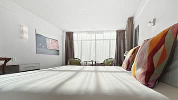 Habitación de hotel con una cama grande, un escritorio, una silla y una mesita. Hay una ventana con cortinas y un cuadro en la pared.