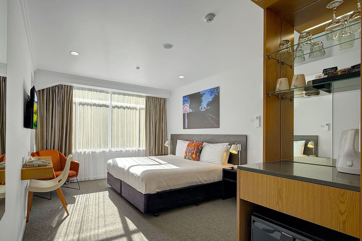A hotel room with a bed, a desk, a chair, a television, and a minibar.