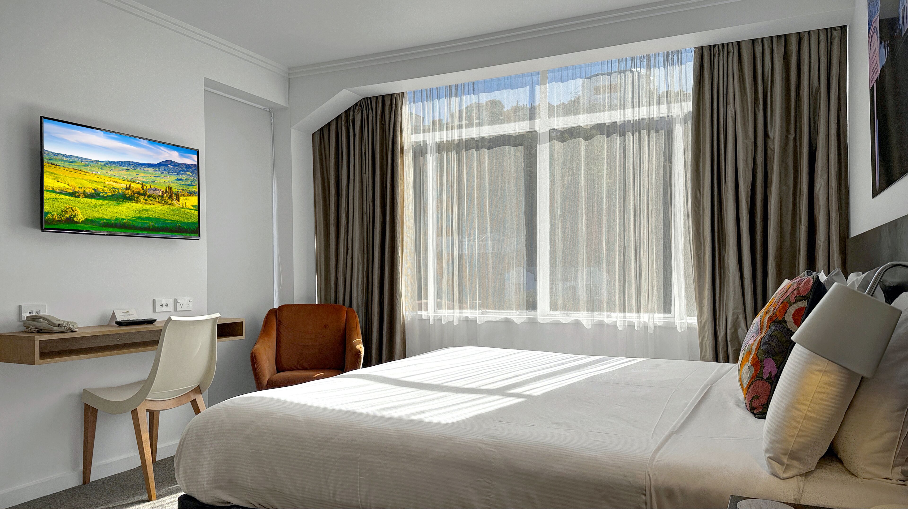 A hotel room with a bed, a desk, a chair, and a large window with curtains.