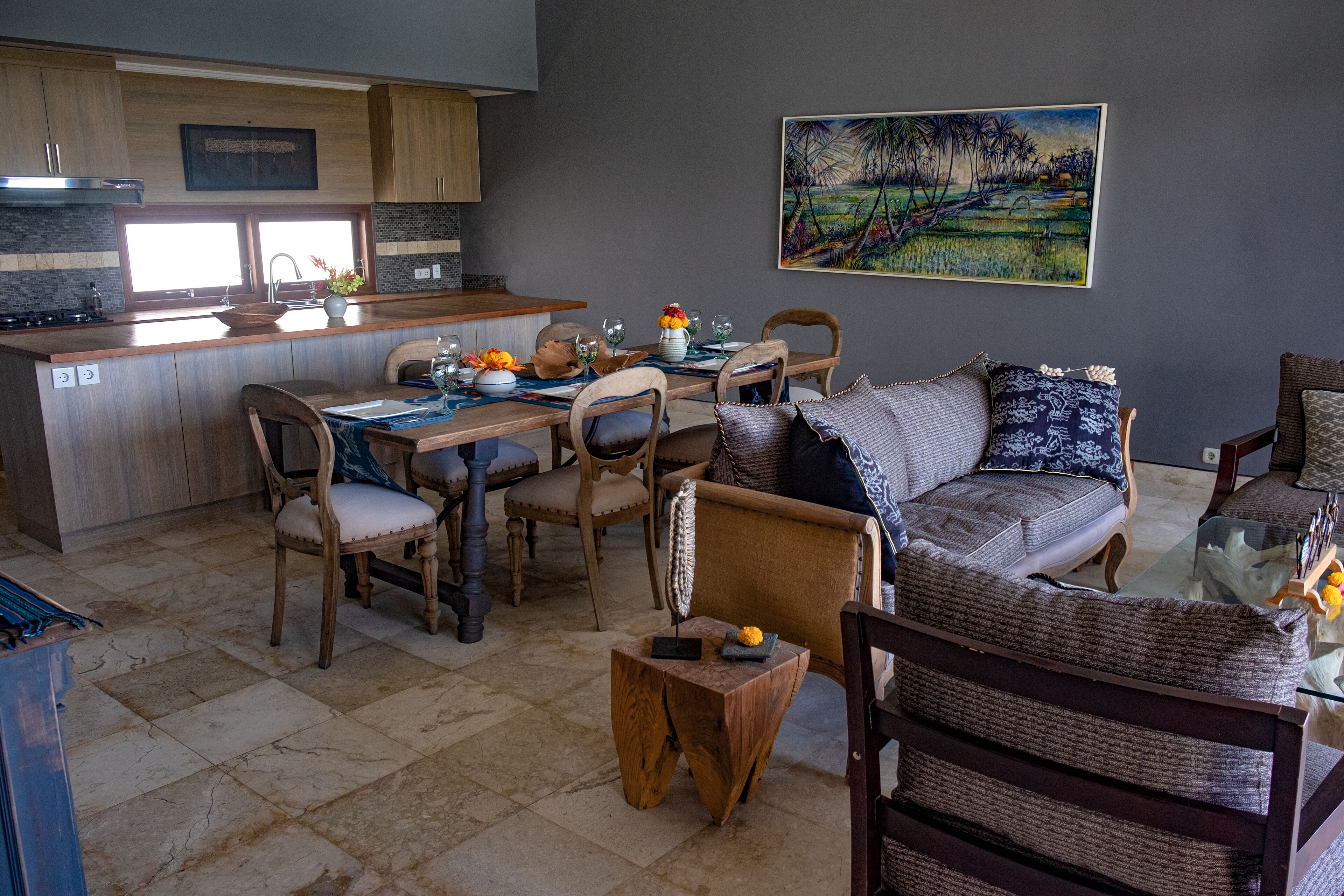 A modern kitchen with wooden cabinets, a dining area with a glass table, and a living room with a sofa and chairs.