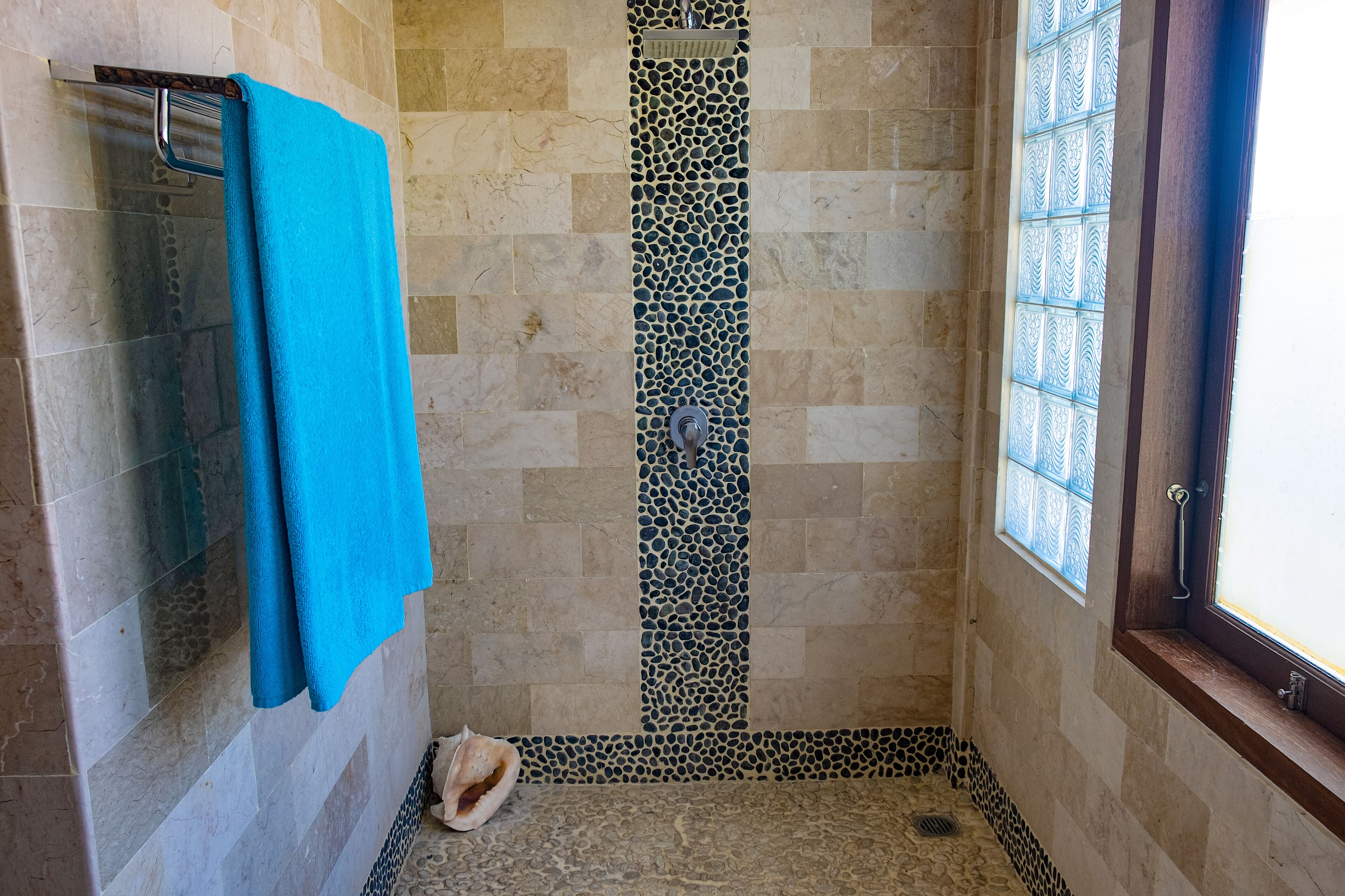 Una ducha con piso de baldosas, una toalla azul colgada en un perchero y un borde decorativo de azulejos.