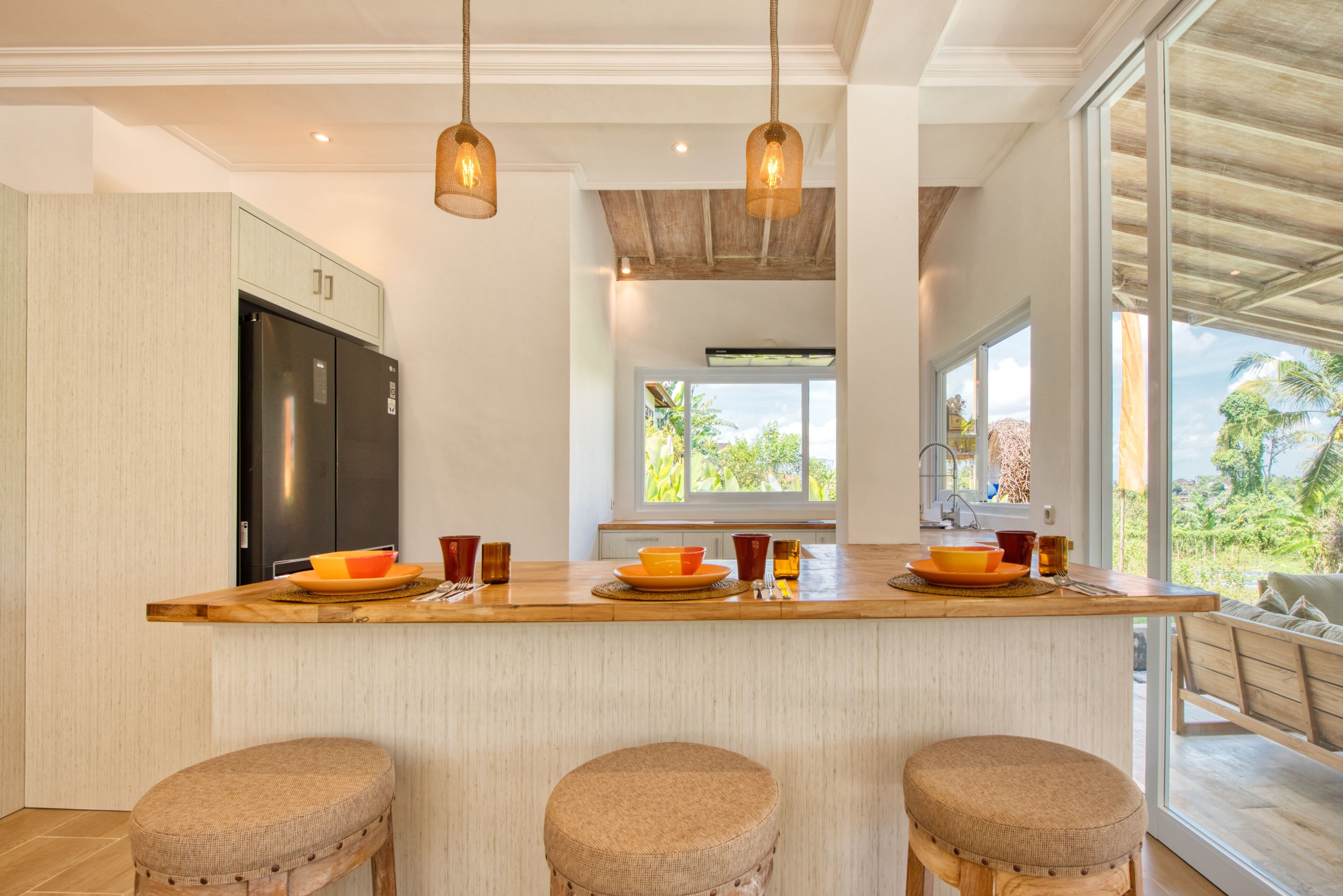 A modern kitchen with a wooden island, bar stools, and a large window offering a view of the outdoors.