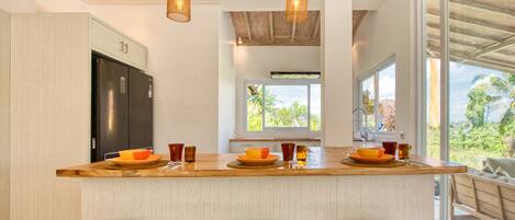 A modern kitchen with a wooden island, bar stools, and a large window offering a view of the outdoors.