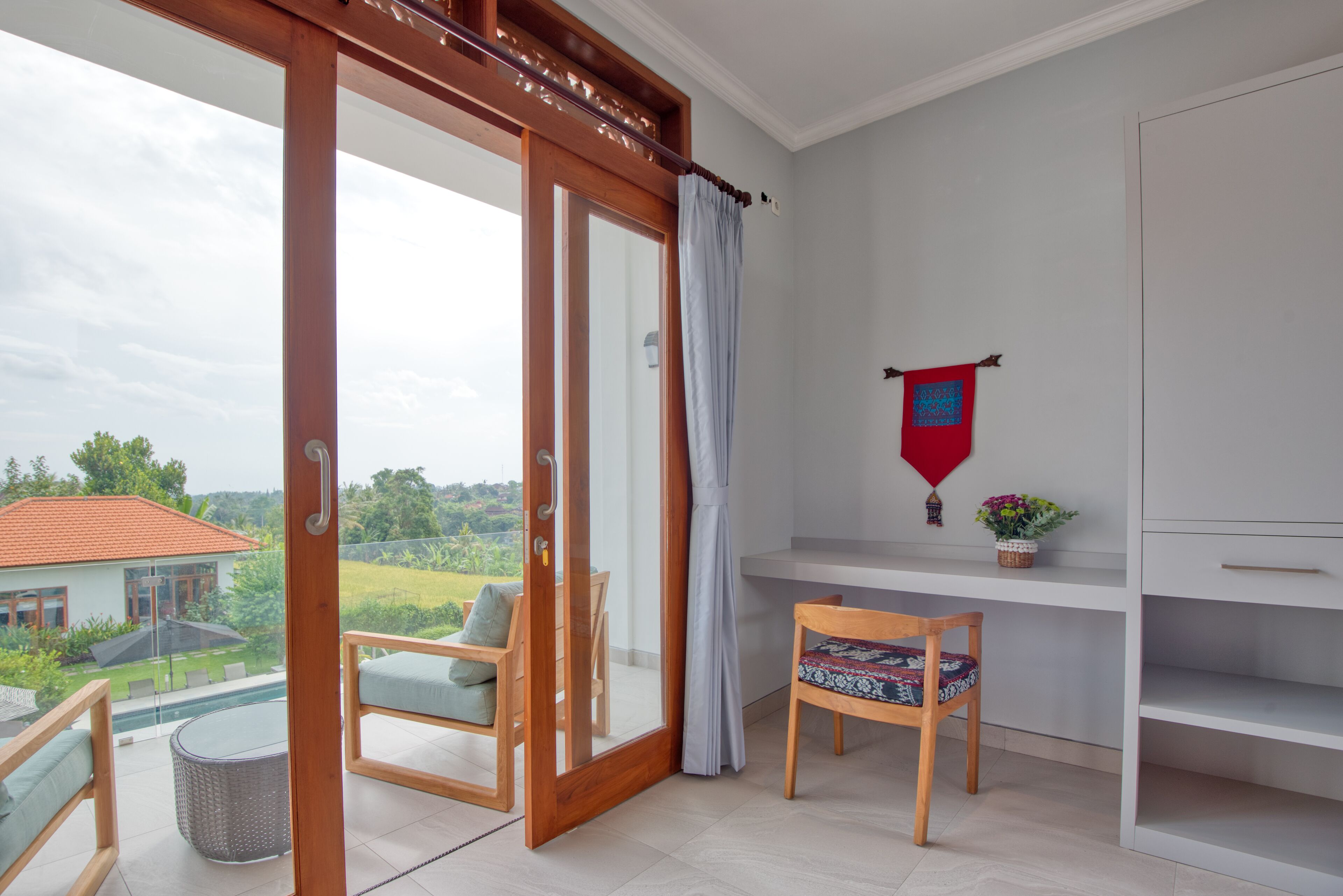 Een balkon met een glazen deur, een houten stoel, een tafeltje en uitzicht op een huis en groen.