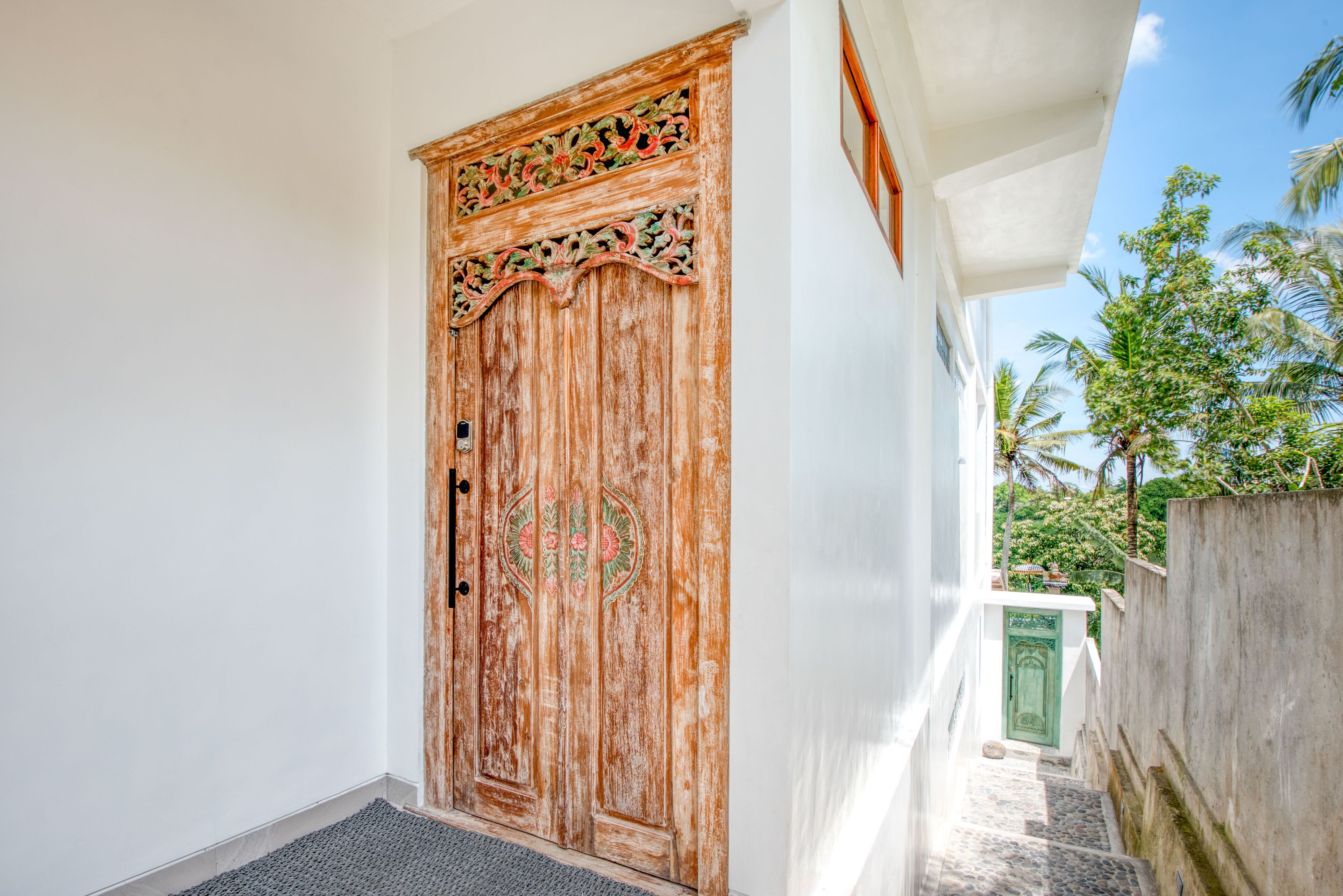 A wooden door with intricate carvings, a concrete wall, and a small staircase leading to a green door.