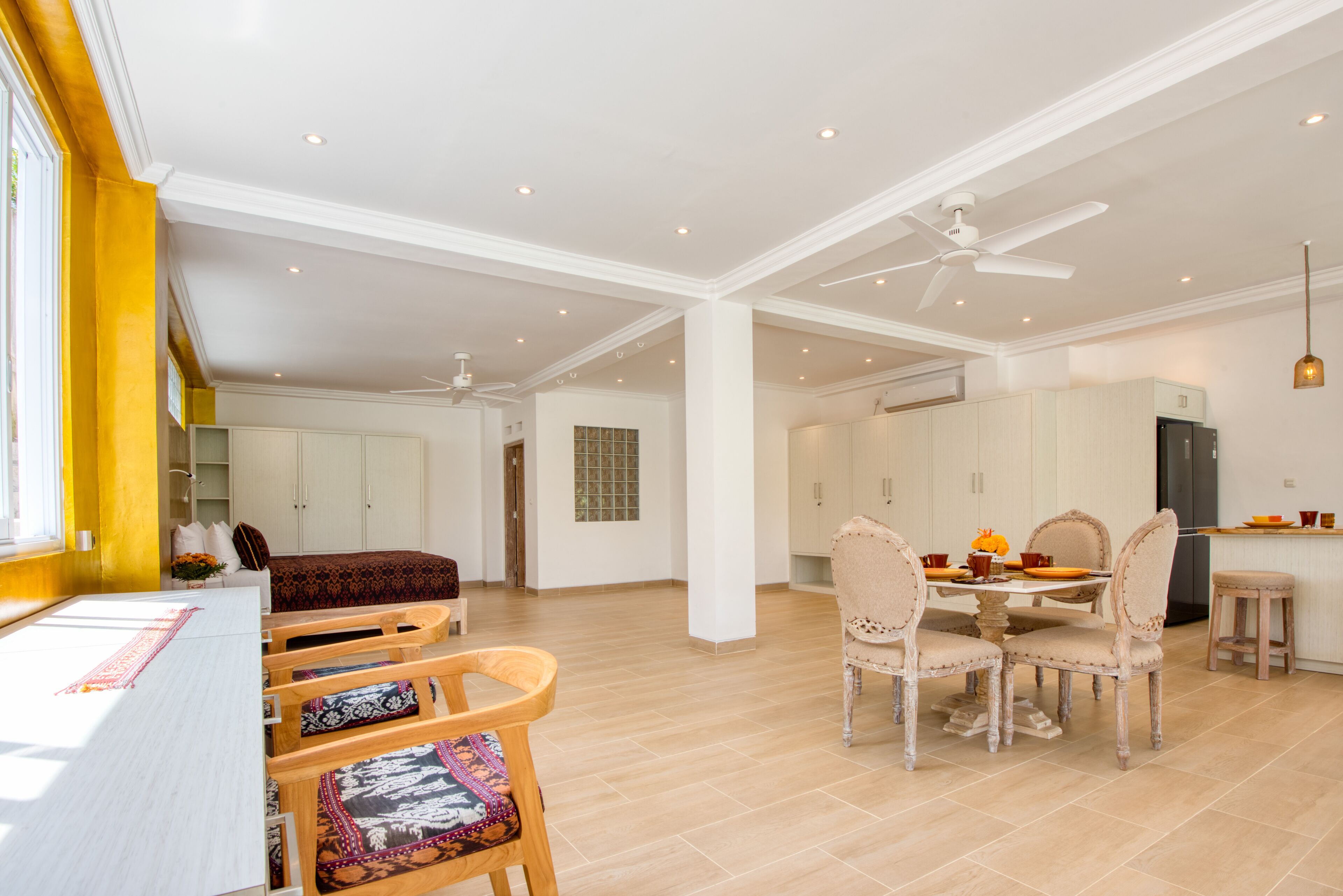 Amplia sala de estar con mesa de comedor, sillas y sofá. Se observa una cocina con armarios y refrigerador.