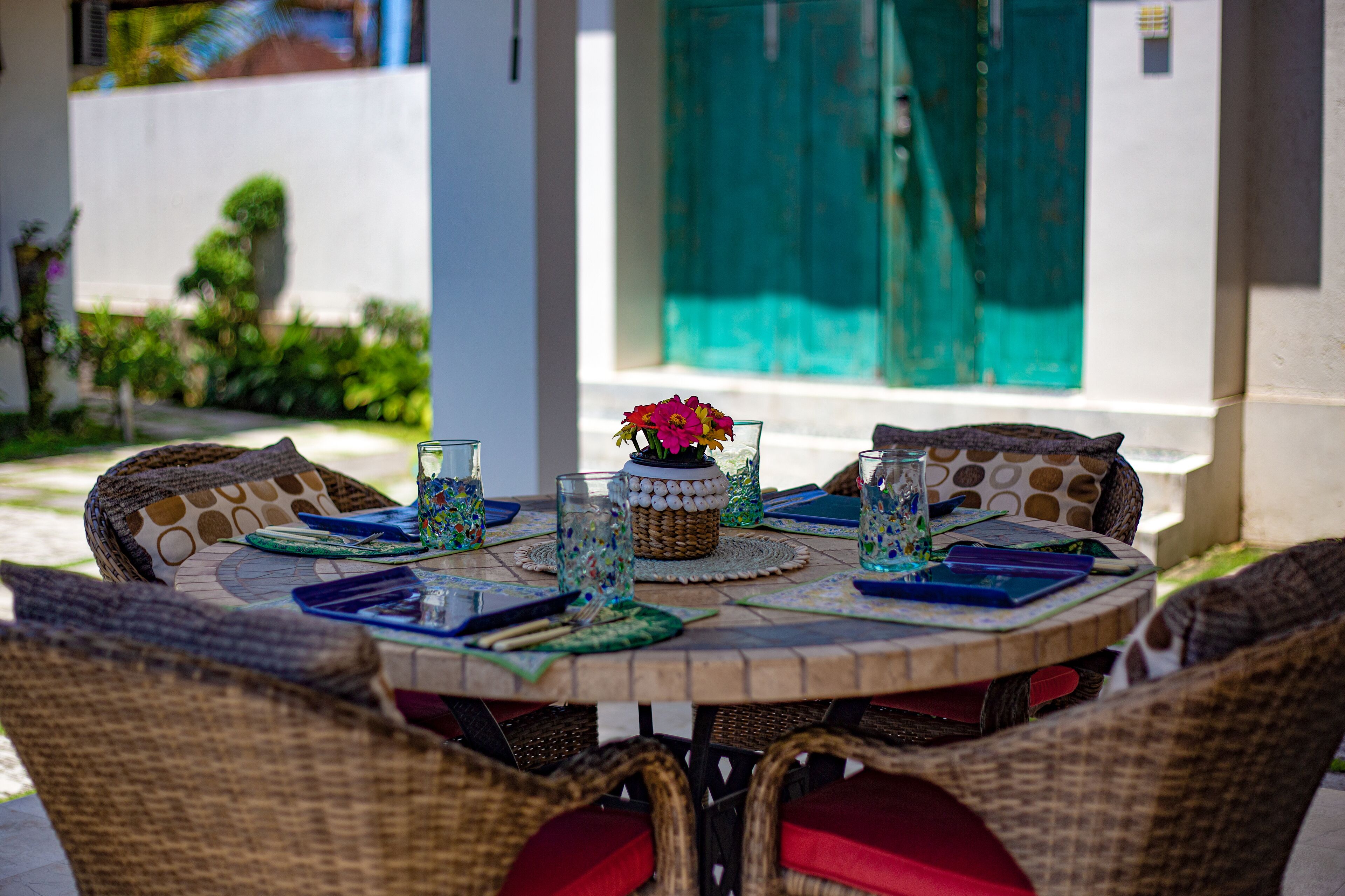A round table with wicker chairs, a woven centerpiece, and blue placemats.
