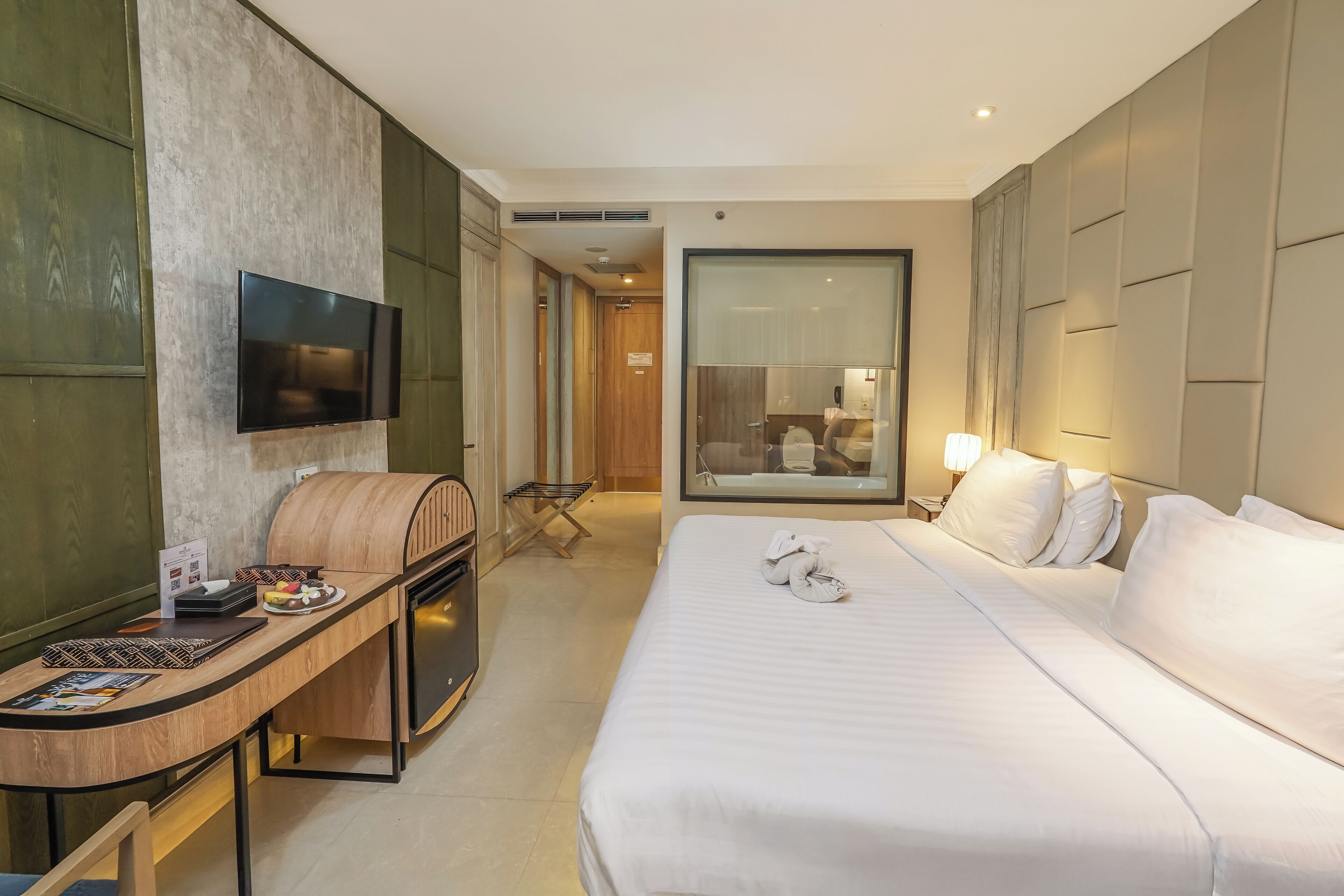 Une chambre d’hôtel comprenant un lit, un bureau avec un téléviseur à écran plat, un banc en bois et une grande fenêtre.