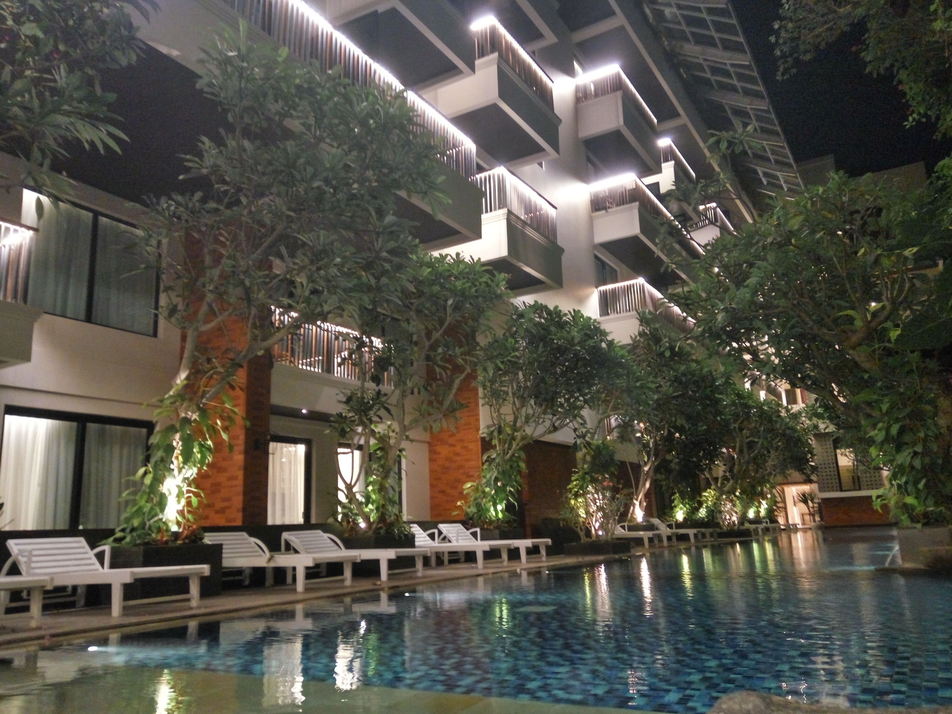 A modern hotel with a pool, lounge chairs, and lush greenery.