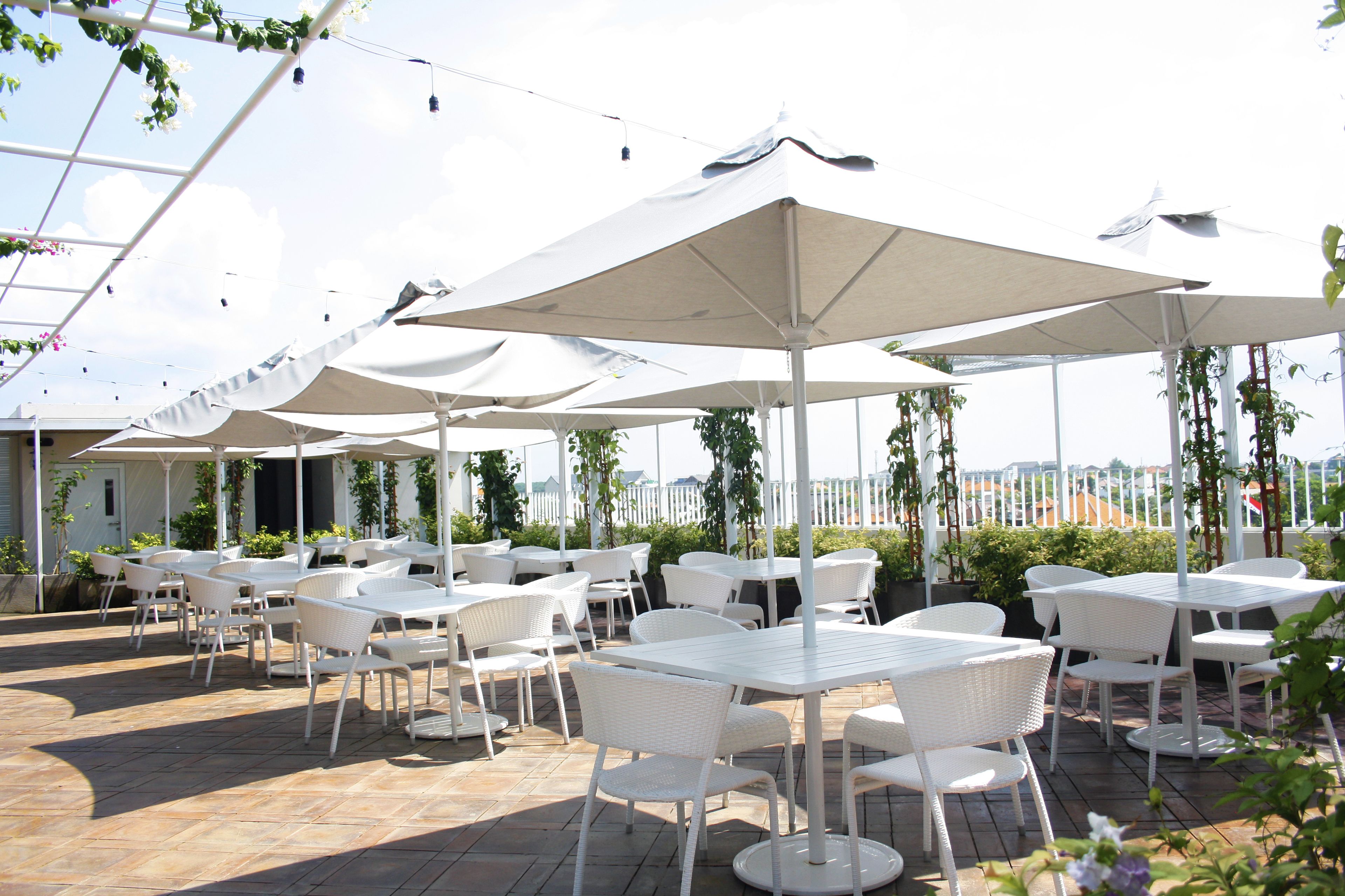 An outdoor patio with white tables and chairs, large umbrellas, and potted plants.