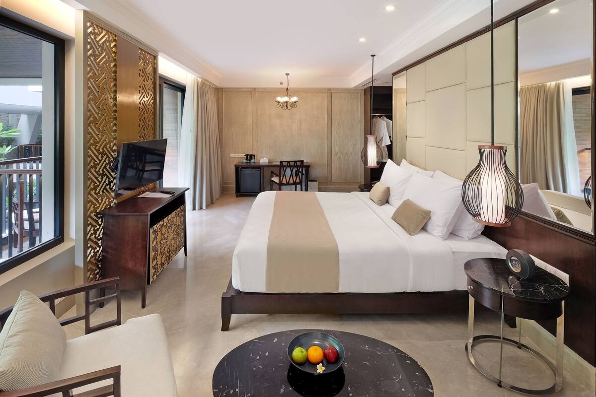 Habitación de hotel con una cama grande, un escritorio con televisor, una zona de comedor y vistas al balcón.