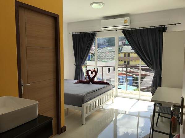 Una habitación de hotel con cama, escritorio, silla, ventana con cortinas y aire acondicionado.