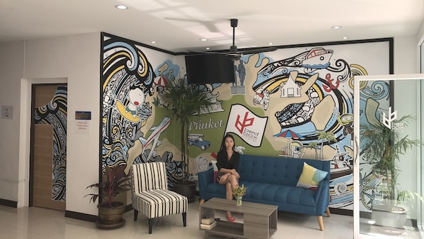 A reception area with a colorful mural, a blue sofa, a striped armchair, and a coffee table. - Bedbox Guesthouse & Hostel (Patong)