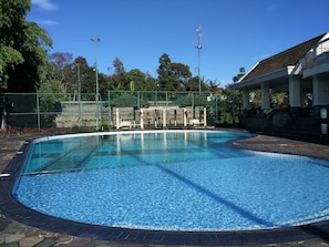 A swimming pool with a tiled deck, surrounded by a fence and trees. - Villa Sabrina Bumi Ciherang (Cipanas)