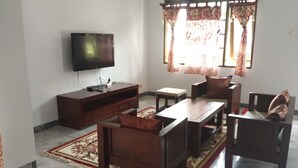 A living room with a TV, wooden furniture, and a patterned rug. - Villa Sabrina Bumi Ciherang (Cipanas)