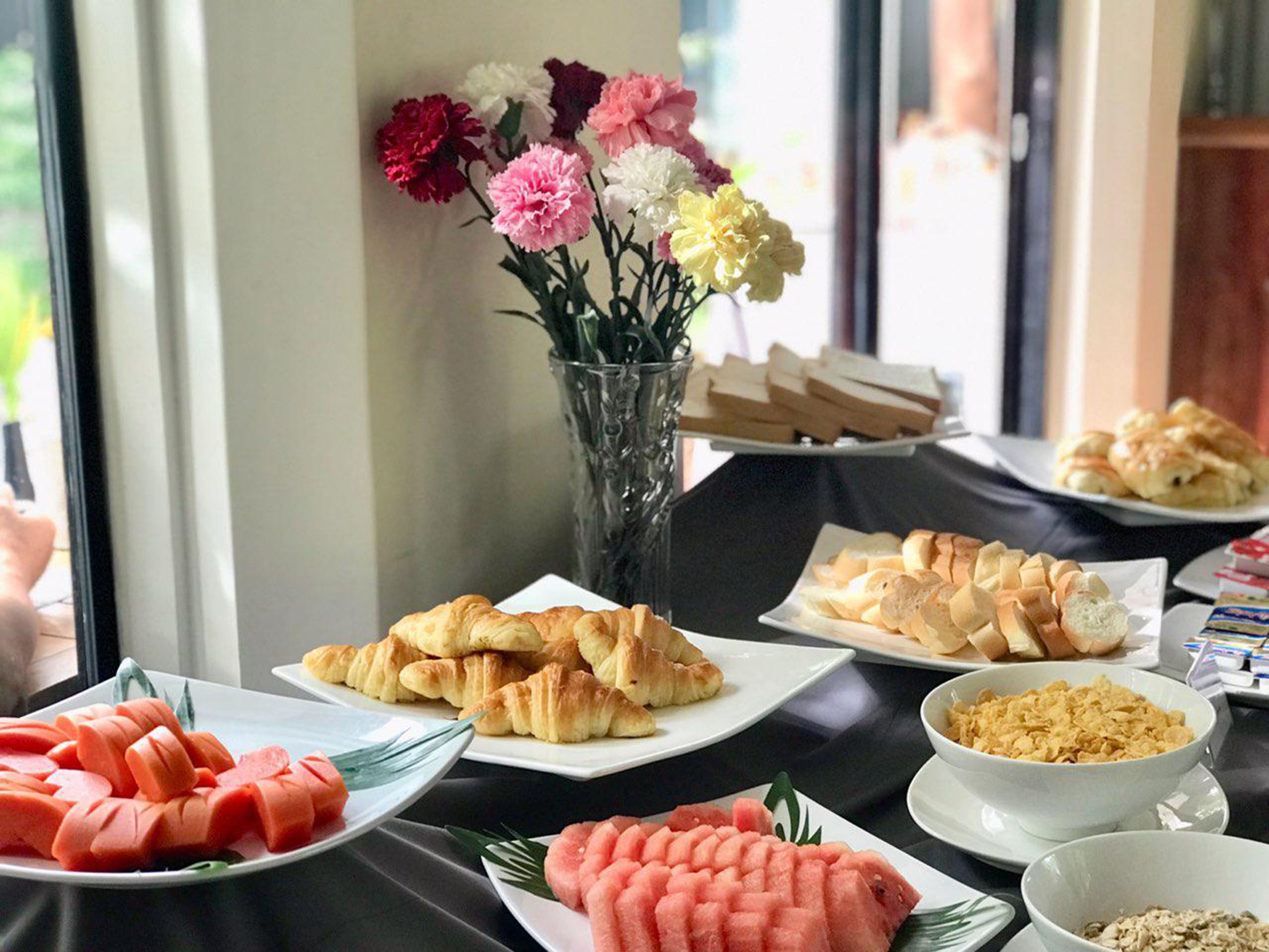 Un bufé de desayuno con cruasanes, sandía, cereales y flores.