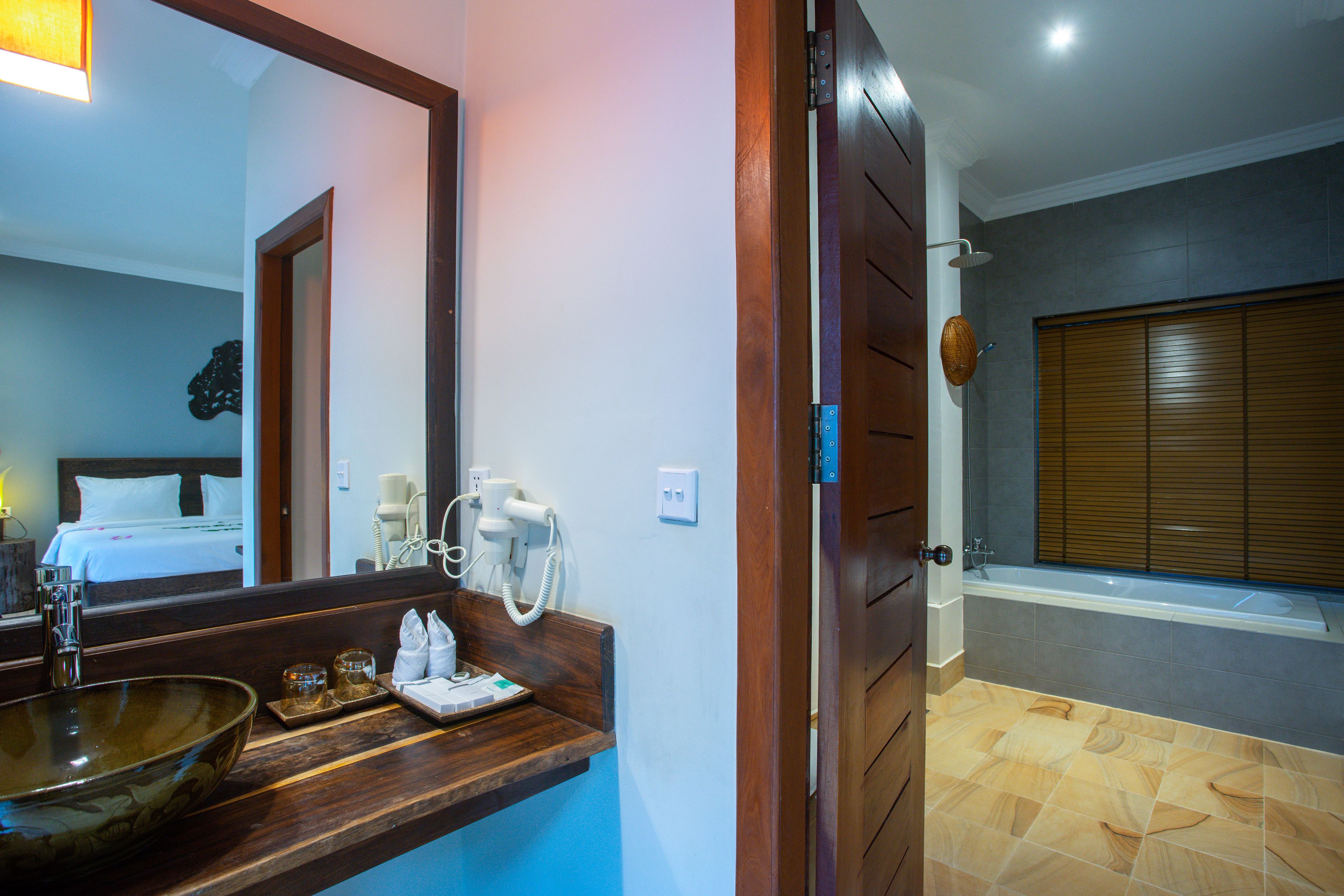 Une salle de bain d’hôtel avec un grand miroir, un meuble-lavabo en bois et une baignoire.