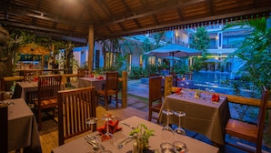 An outdoor restaurant with wooden tables and chairs, surrounded by greenery and a pool. - GZ Angkor Boutique (Siem Reap)