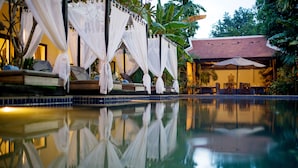 A serene pool area with a clear reflection, surrounded by lush greenery and a traditional building with a tiled roof. - GZ Angkor Boutique (Siem Reap)