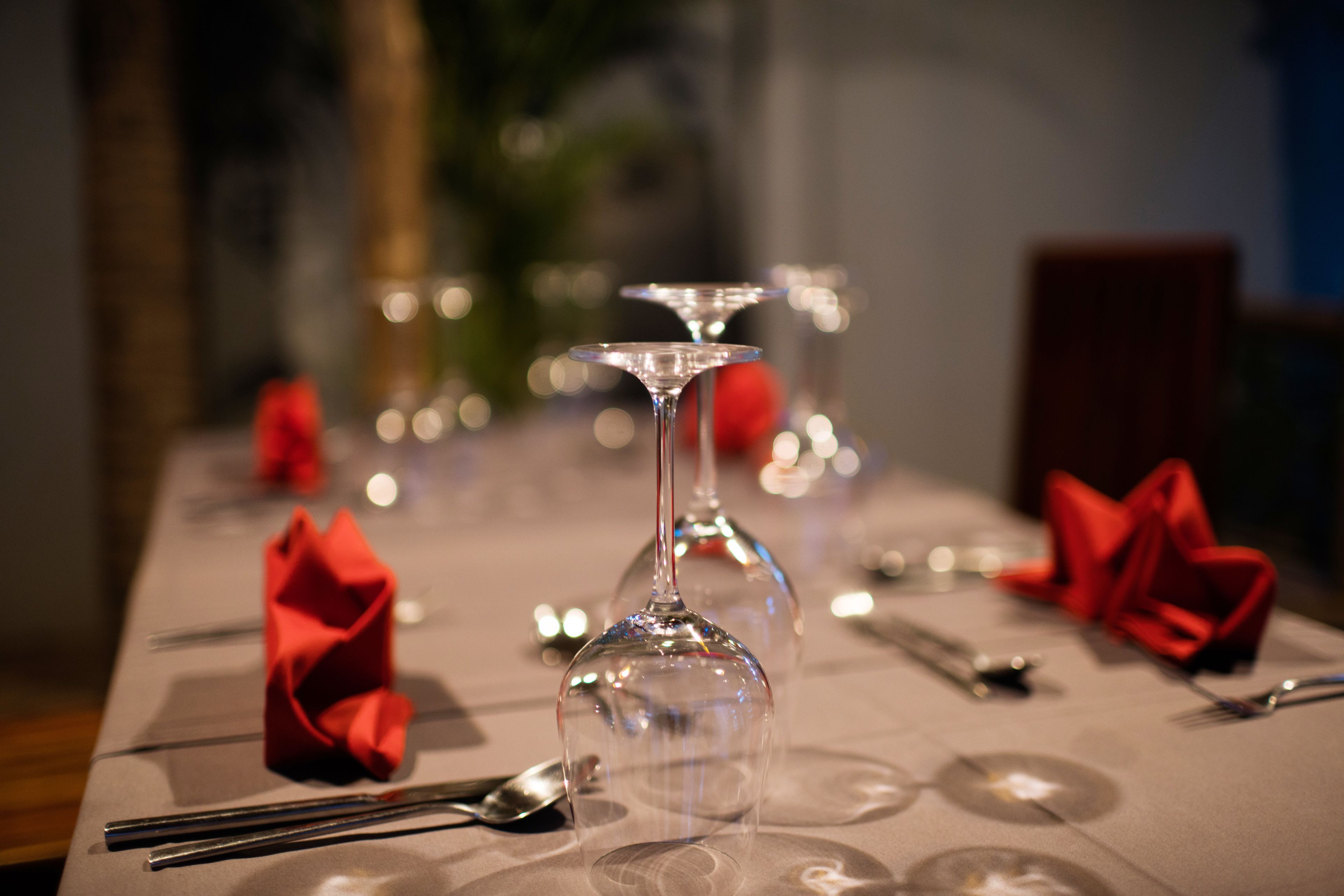 A dining table set with wine glasses, red napkins, and cutlery.