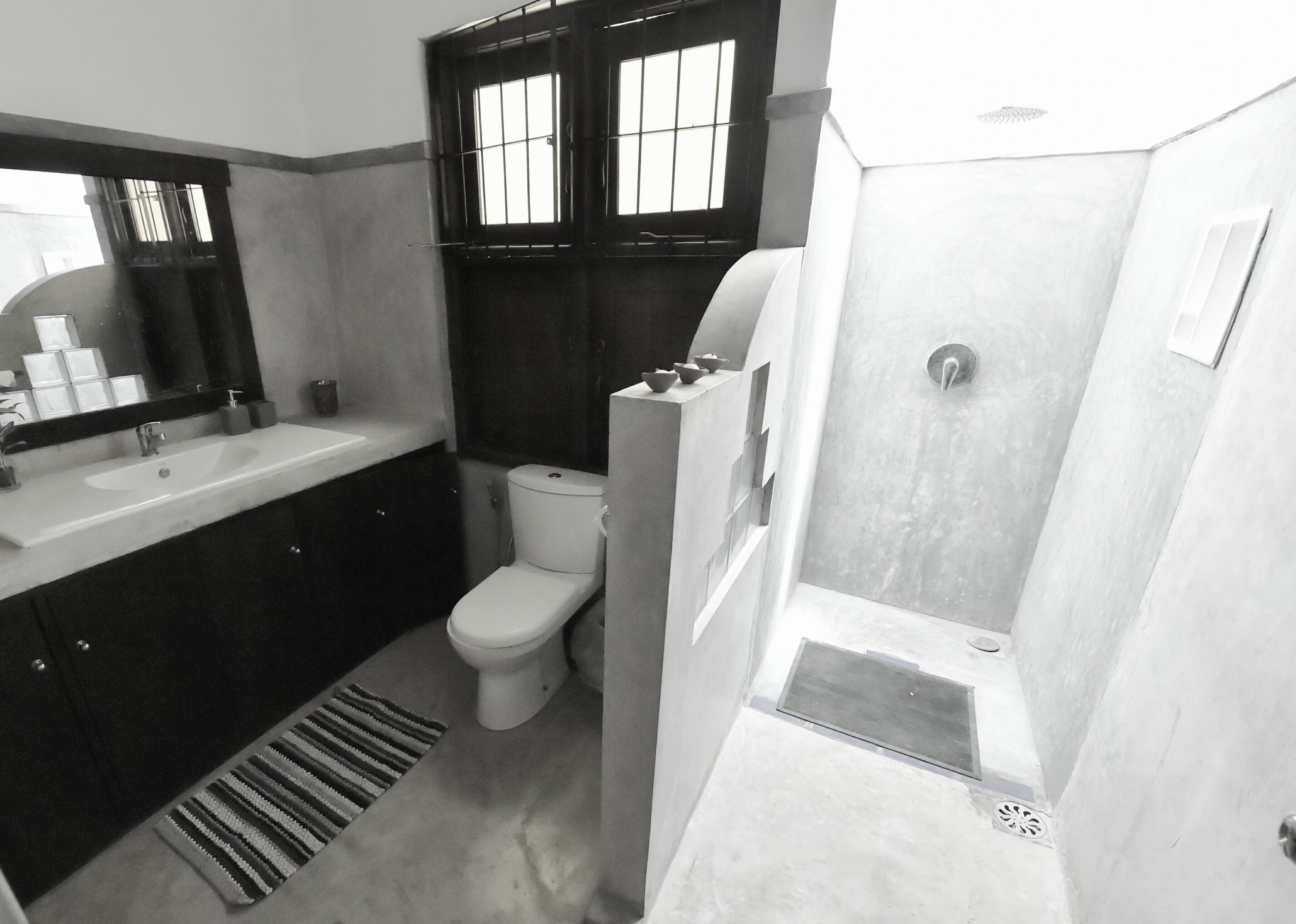 A compact bathroom with a white sink, dark cabinets, a toilet, and a shower area.